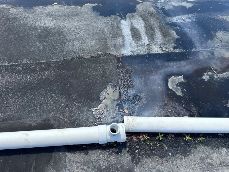 Disconnected HVAC drain line on a commercial rooftop with visible water stains and algae buildup, indicating overflow and drainage issues