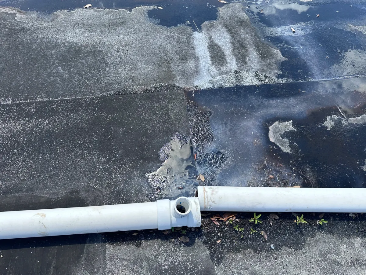 Disconnected HVAC drain line on a commercial rooftop with visible water stains and algae buildup, indicating overflow and drainage issues